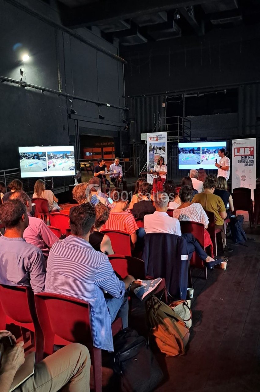 Un groupe de personnes assises dans une salle sombre, regardant une présentation projetée sur plusieurs écrans.