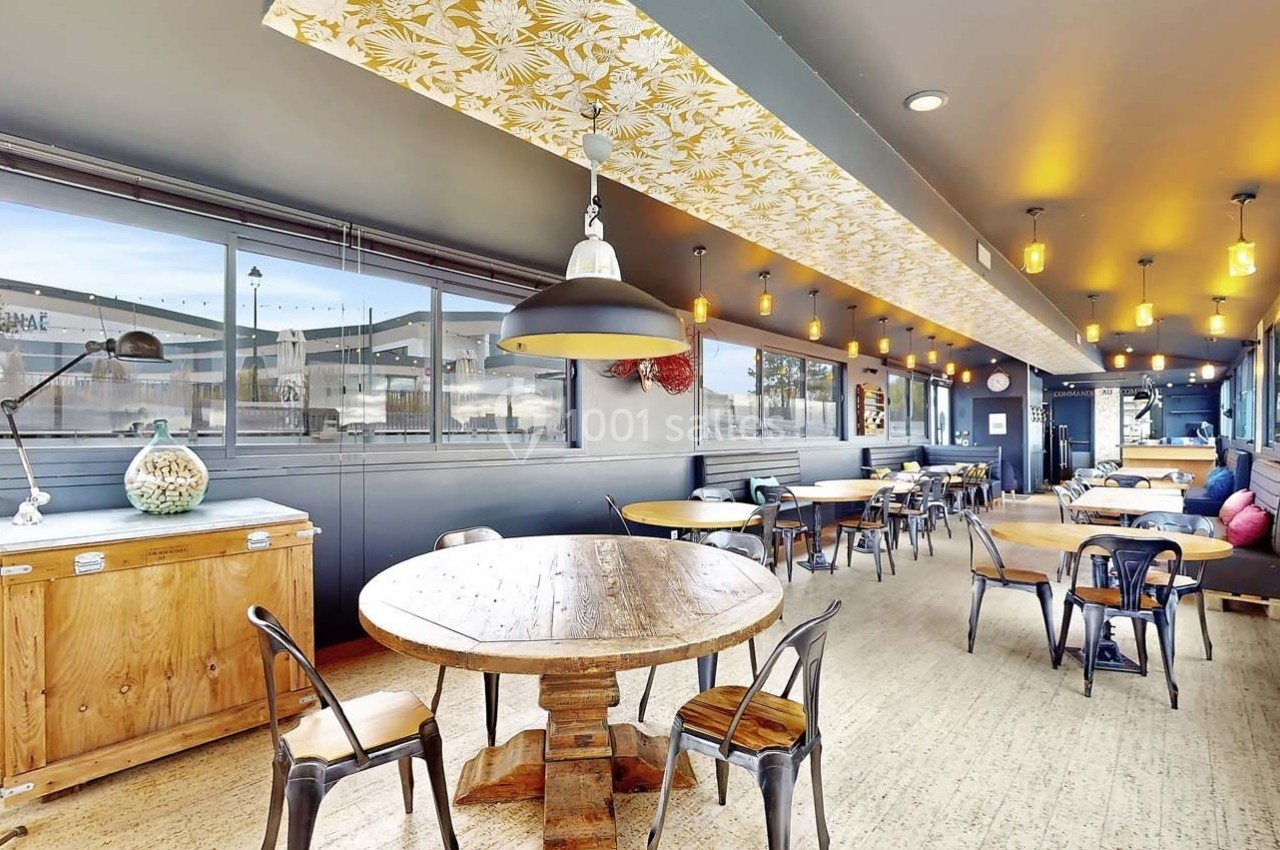 Salle de restaurant lumineuse avec tables en bois, chaises métalliques et plafond décoré d'un motif floral.