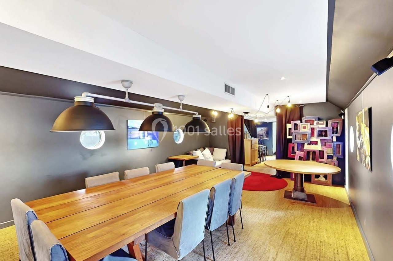 Salle moderne avec grande table en bois, chaises grises, luminaires suspendus et décorations murales colorées.