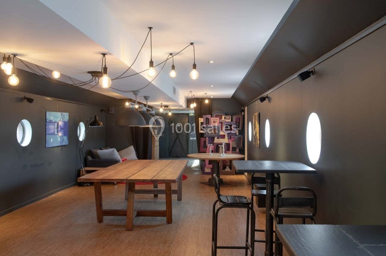 Salle moderne avec tables en bois, chaises noires, éclairage suspendu et décorations murales colorées.