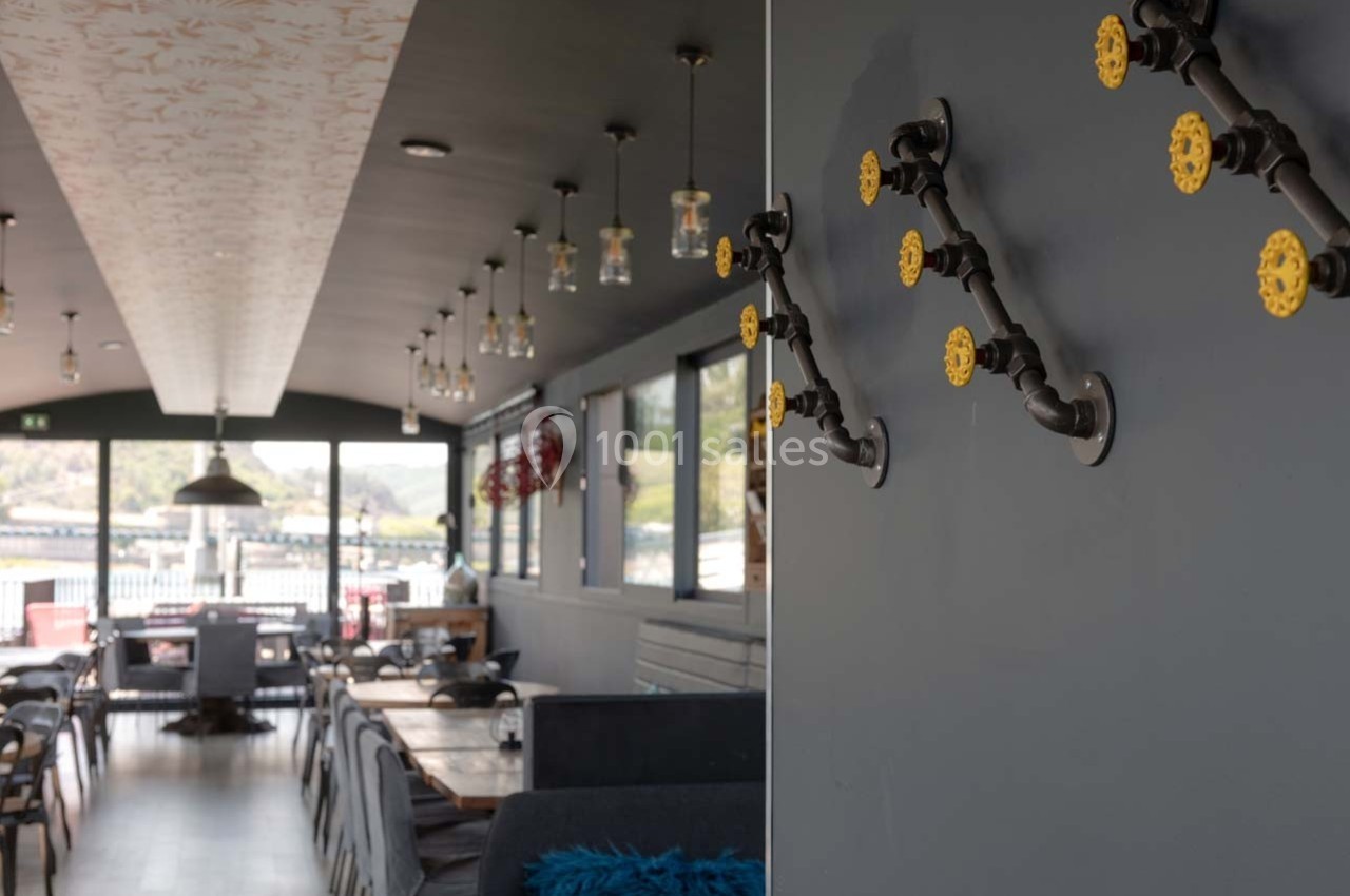 Intérieur d'un restaurant moderne avec des tables en bois, des suspensions lumineuses et des décorations murales en tuyaux.
