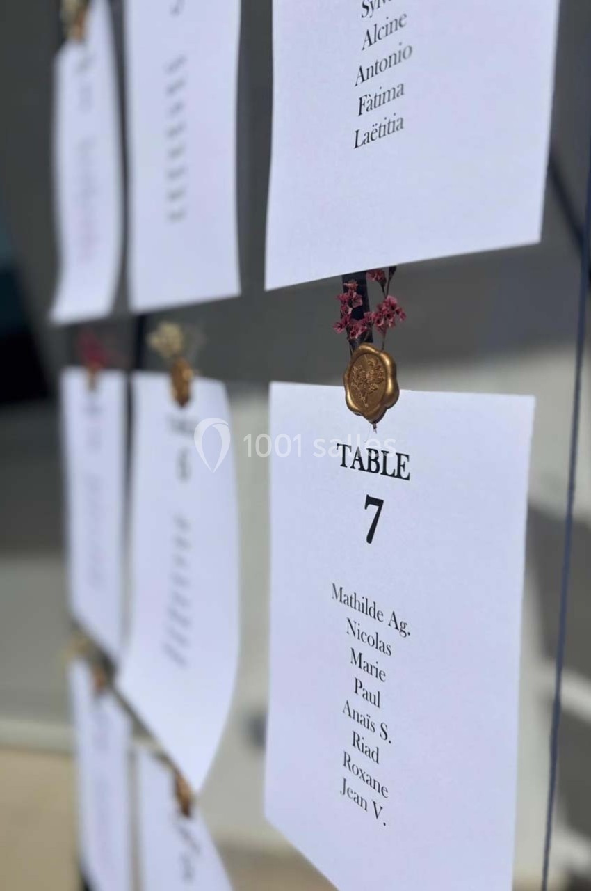 Liste des invités pour la table 7, affichée sur un panneau avec des sceaux décoratifs et des fleurs séchées.