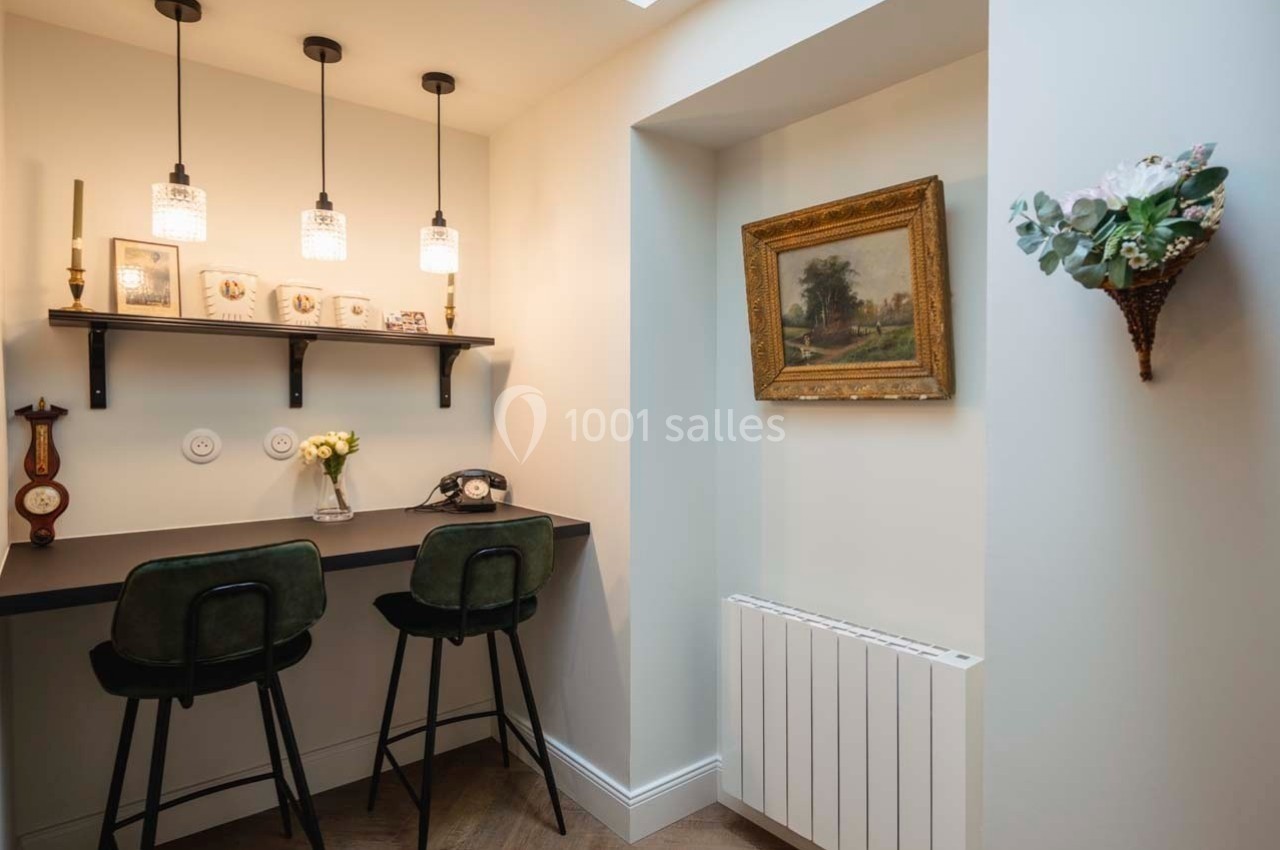 Coin bureau avec deux chaises hautes, étagère murale décorée, éclairage suspendu et tableau encadré sur le mur.