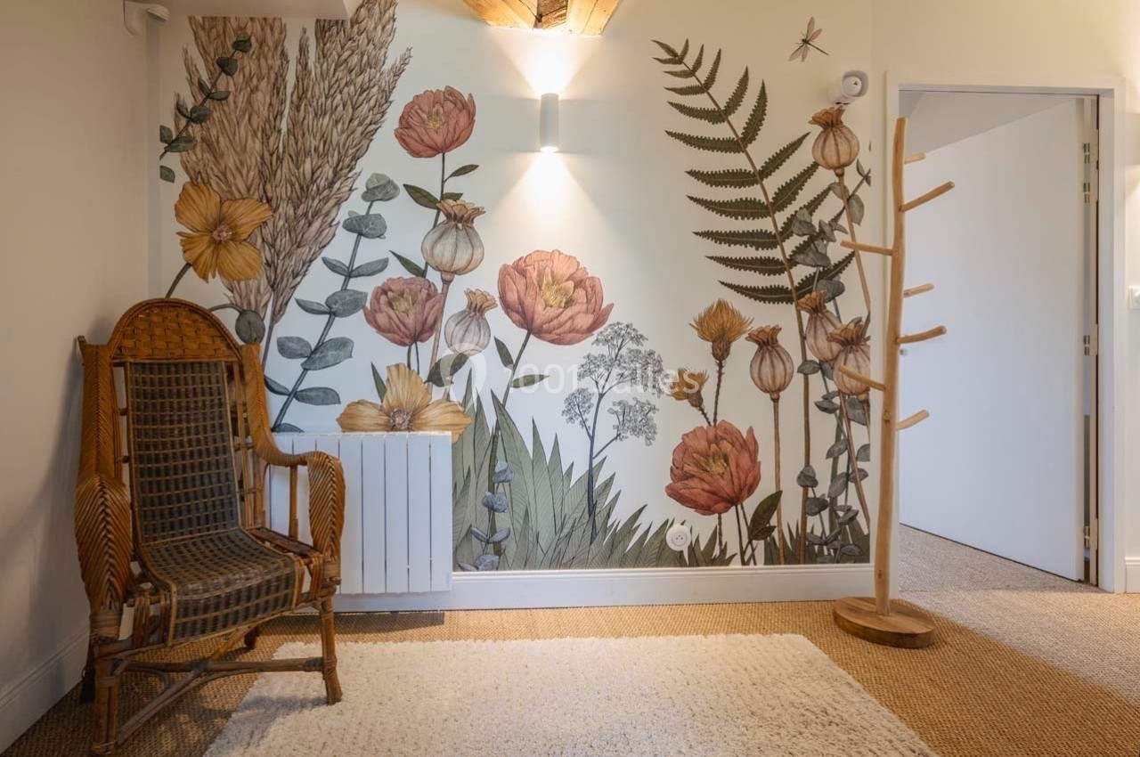 Fresque murale florale avec des motifs de plantes et fleurs, chaise en osier et porte-manteau en bois dans une pièce…