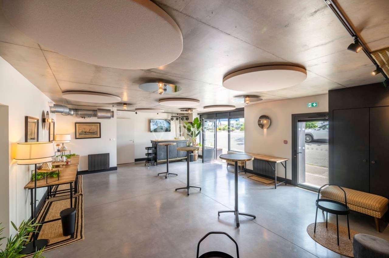 Salle lumineuse avec tables hautes, chaises, décor moderne et panneaux acoustiques au plafond.