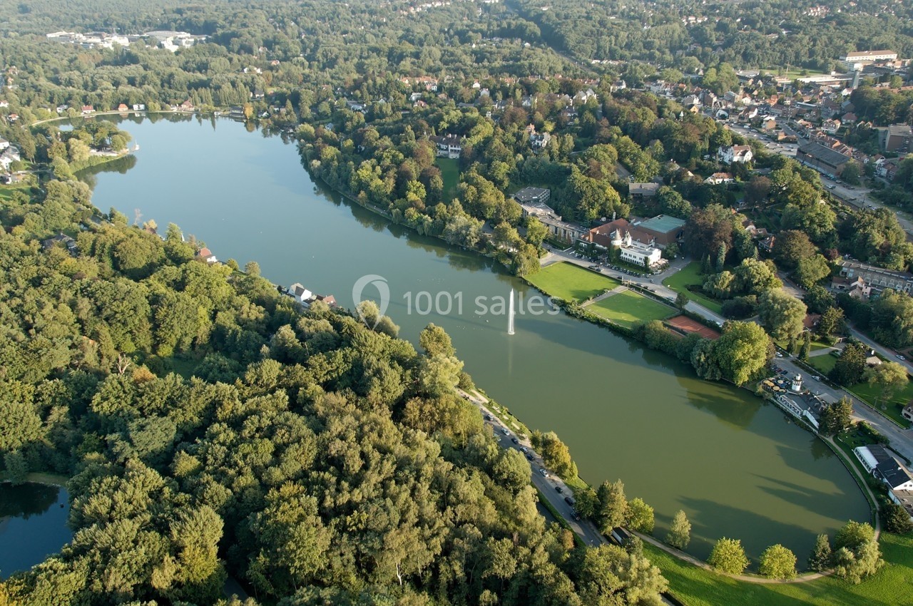 Vue aérienne d'un lac entouré de forêts, de maisons et d'espaces verts dans un paysage urbain et naturel.