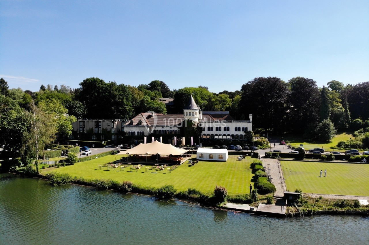 Vue aérienne d'un domaine avec un bâtiment principal, une tente, une pelouse et un plan d'eau au premier plan.