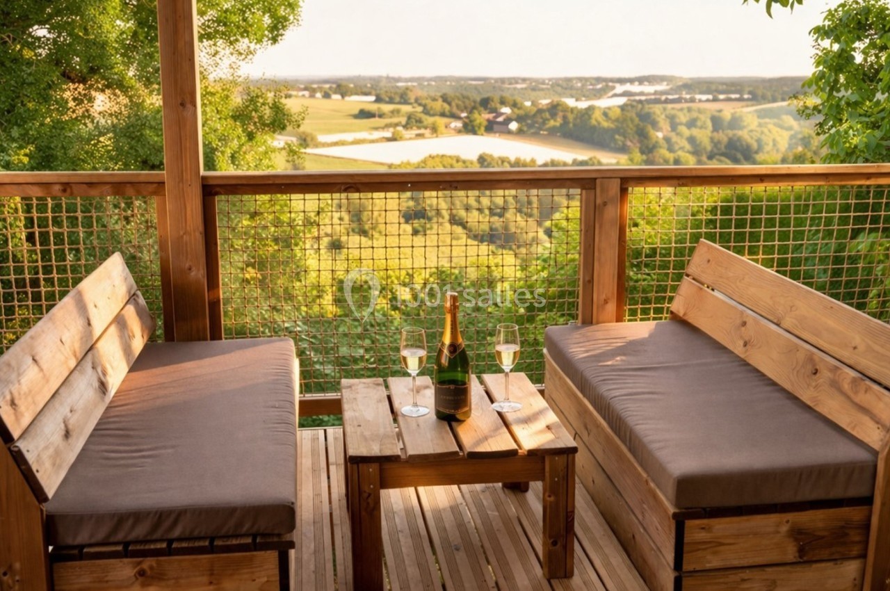 Terrasse en bois avec deux bancs, une table basse, une bouteille de champagne et vue sur une campagne verdoyante.