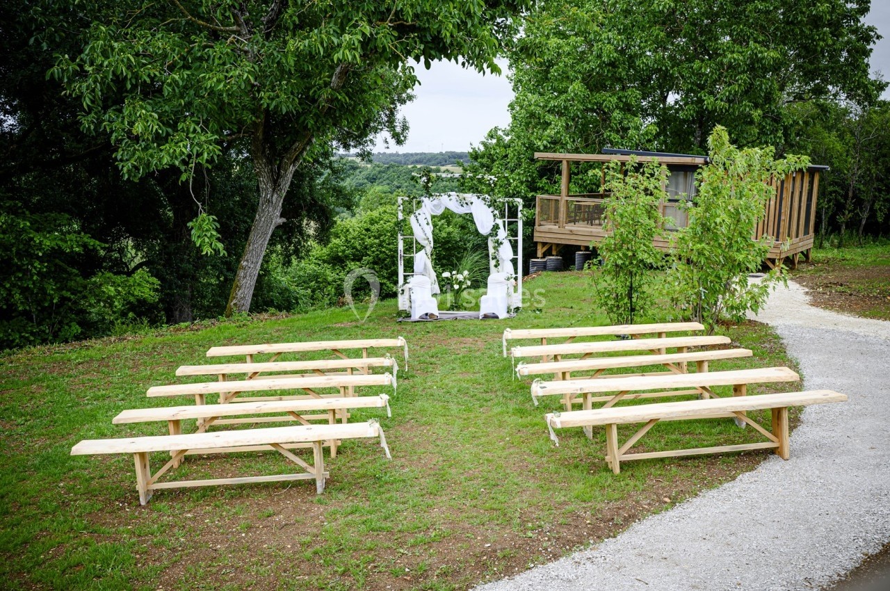 Disposition de bancs en bois face à une arche de mariage décorée, dans un cadre extérieur verdoyant.