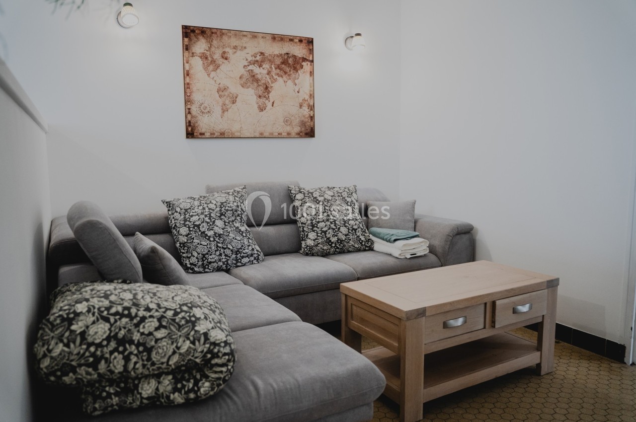 Canapé d'angle gris avec coussins à motifs, table basse en bois clair et carte du monde encadrée au mur.