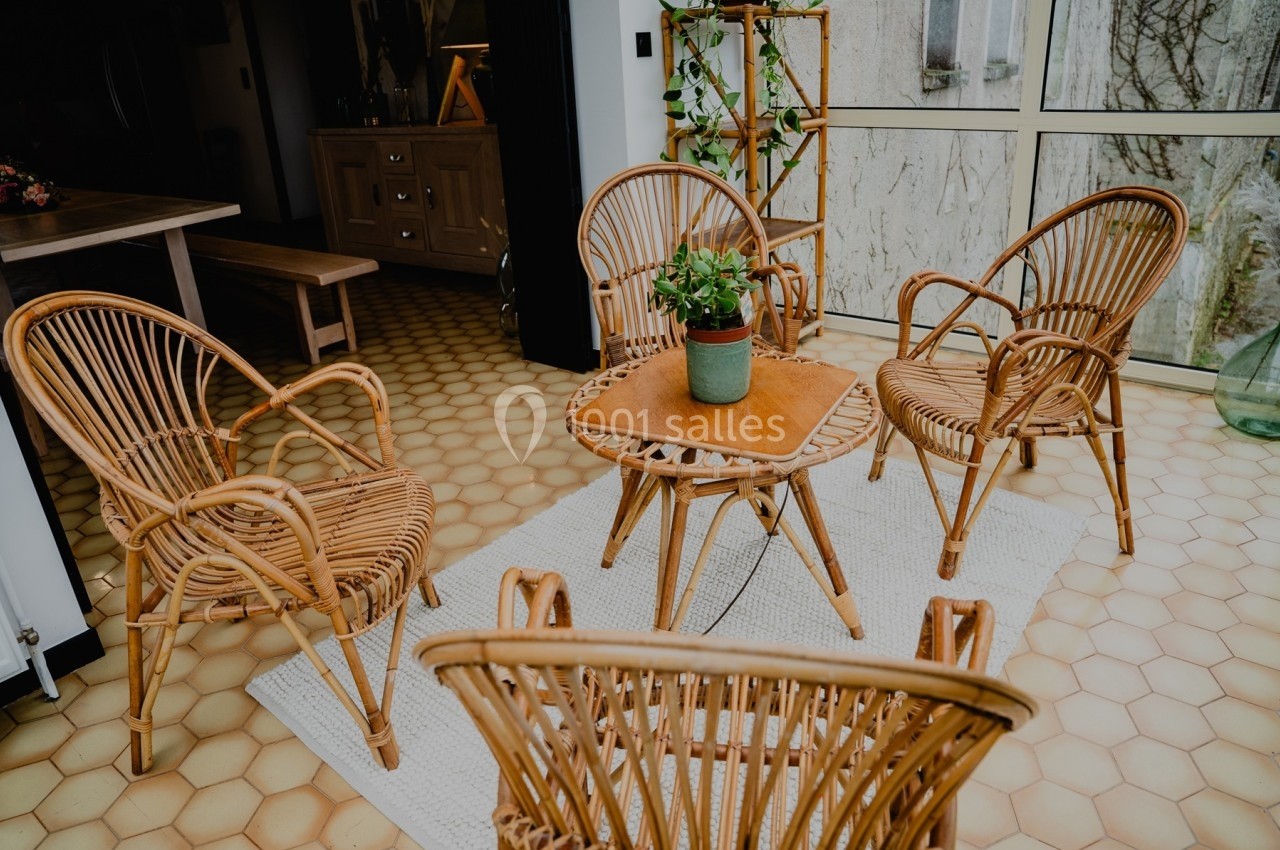 Mobilier en rotin disposé autour d'une table basse avec une plante, dans une pièce lumineuse au sol en carrelage hexagonal.