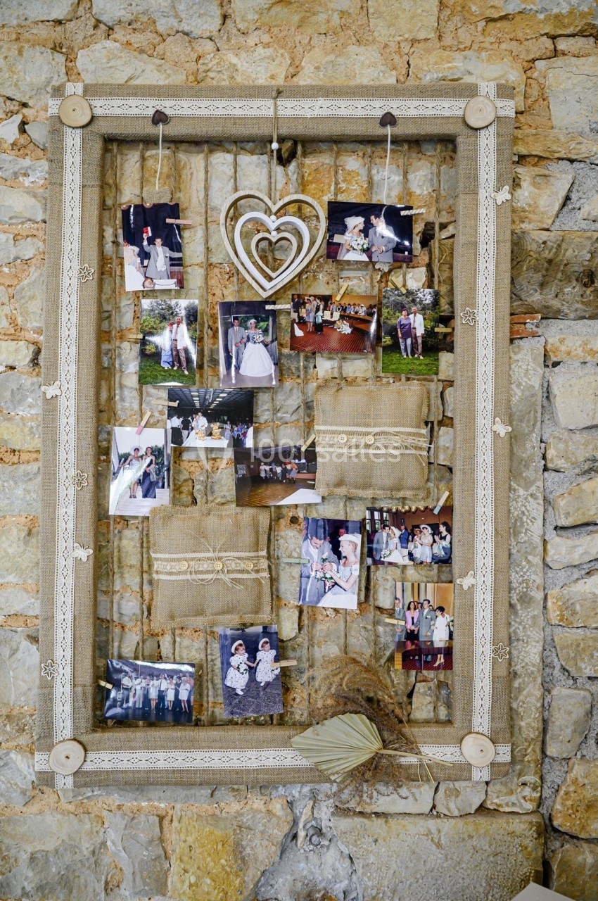 Cadre en bois décoratif suspendu à un mur en pierre, contenant des photos et des ornements en tissu et corde.