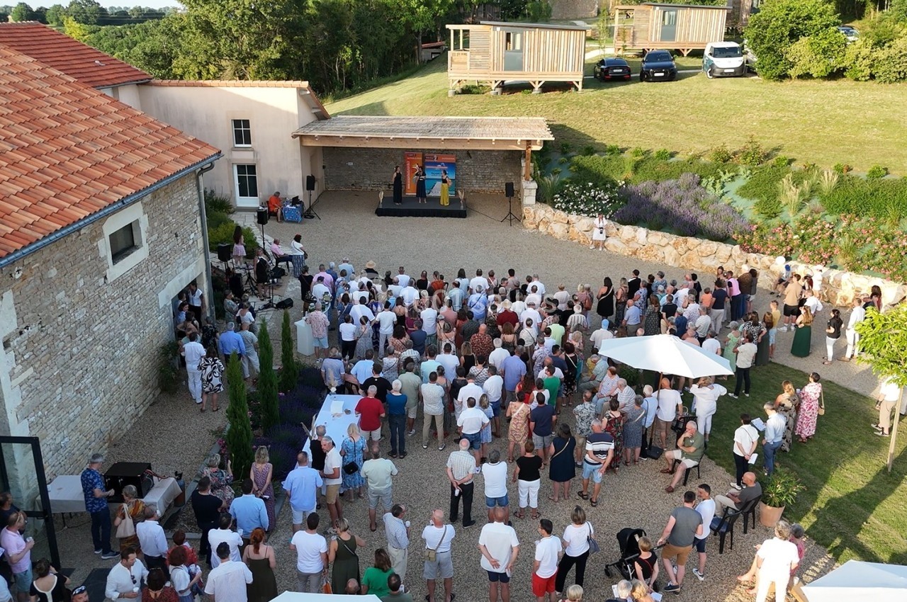 Vue aérienne d'un rassemblement en plein air dans une cour, avec une scène et des spectateurs debout.