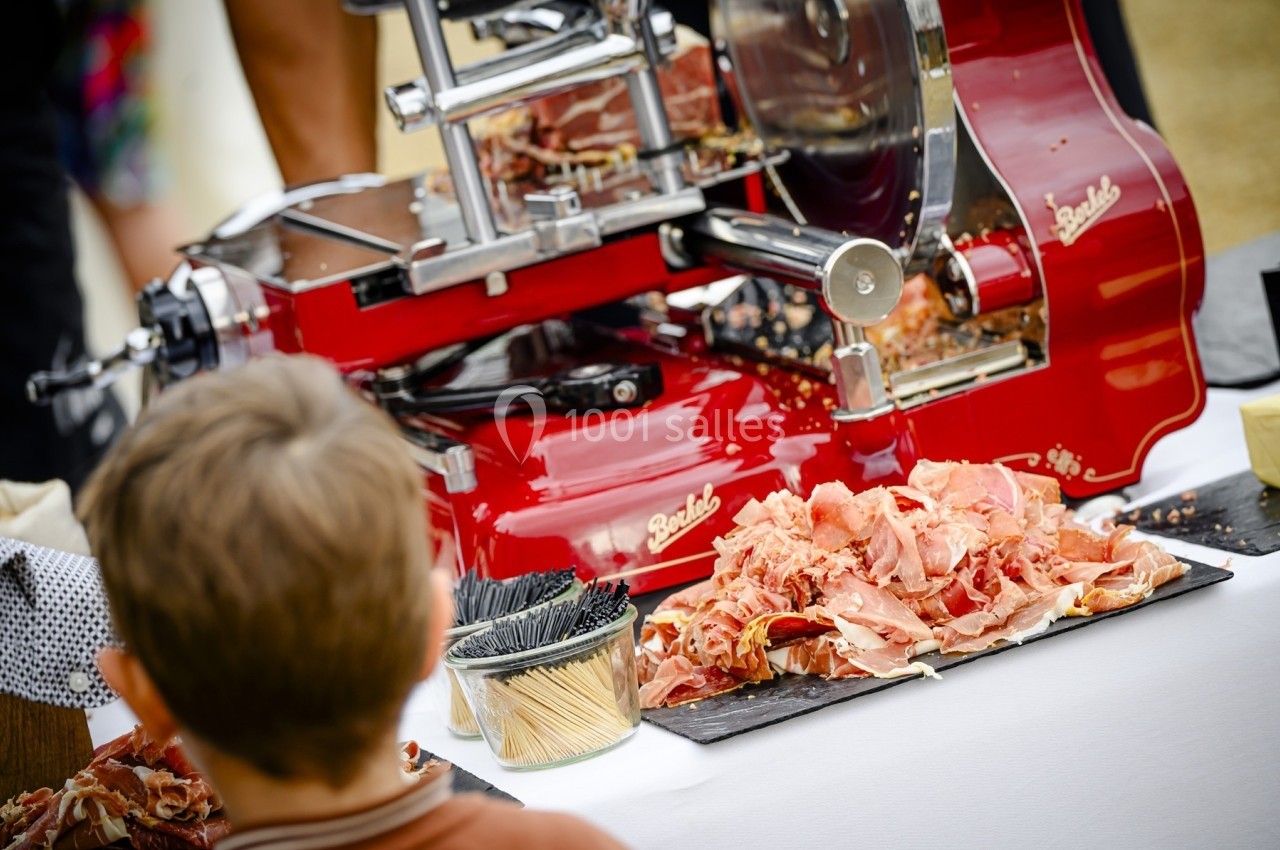 Trancheuse rouge en action avec des tranches de jambon déposées sur une table, vue partielle d'un enfant au premier plan.