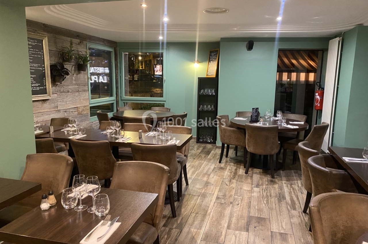Salle de restaurant moderne avec tables dressées, chaises en cuir marron et décoration sobre dans des tons verts et bois.
