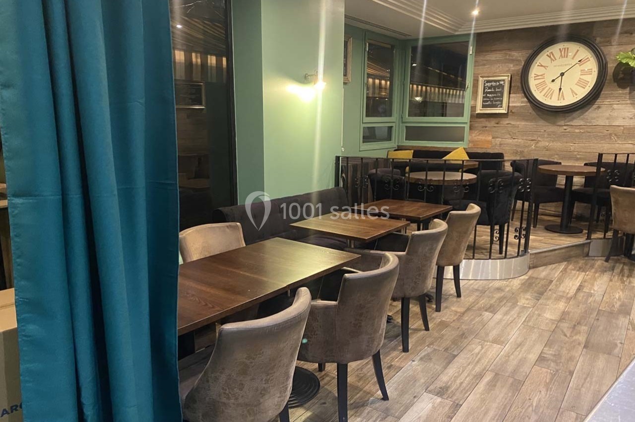 Salle de restaurant avec tables en bois, chaises rembourrées, mur en bois, horloge murale et rideau turquoise.