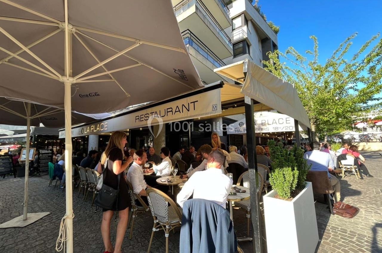 Terrasse d'un restaurant bondée, avec des clients attablés sous des parasols par une journée ensoleillée.