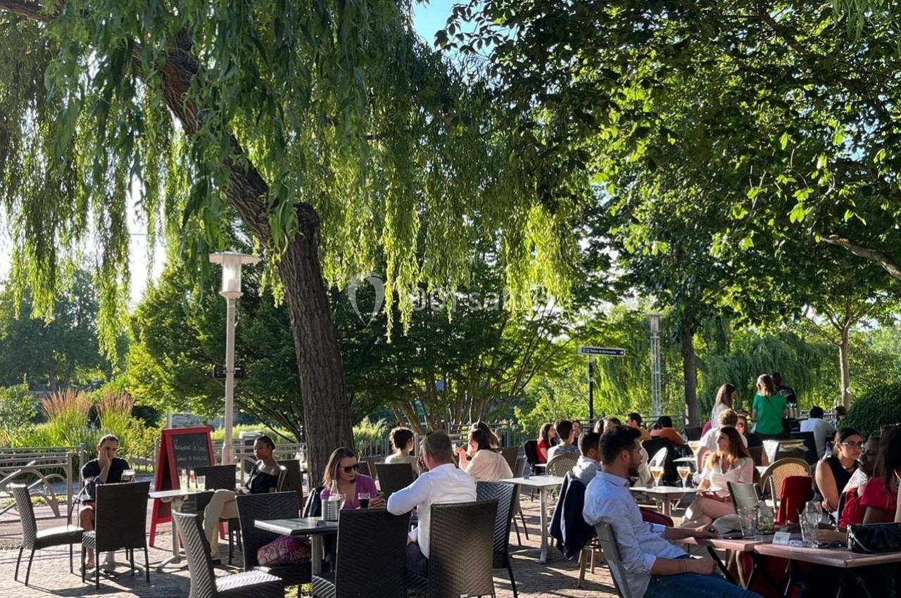 Terrasse extérieure ombragée avec des tables occupées par des personnes profitant d'un repas par temps ensoleillé.
