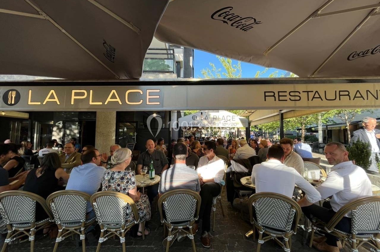Terrasse animée d'un restaurant avec des clients assis sous des parasols par une journée ensoleillée.