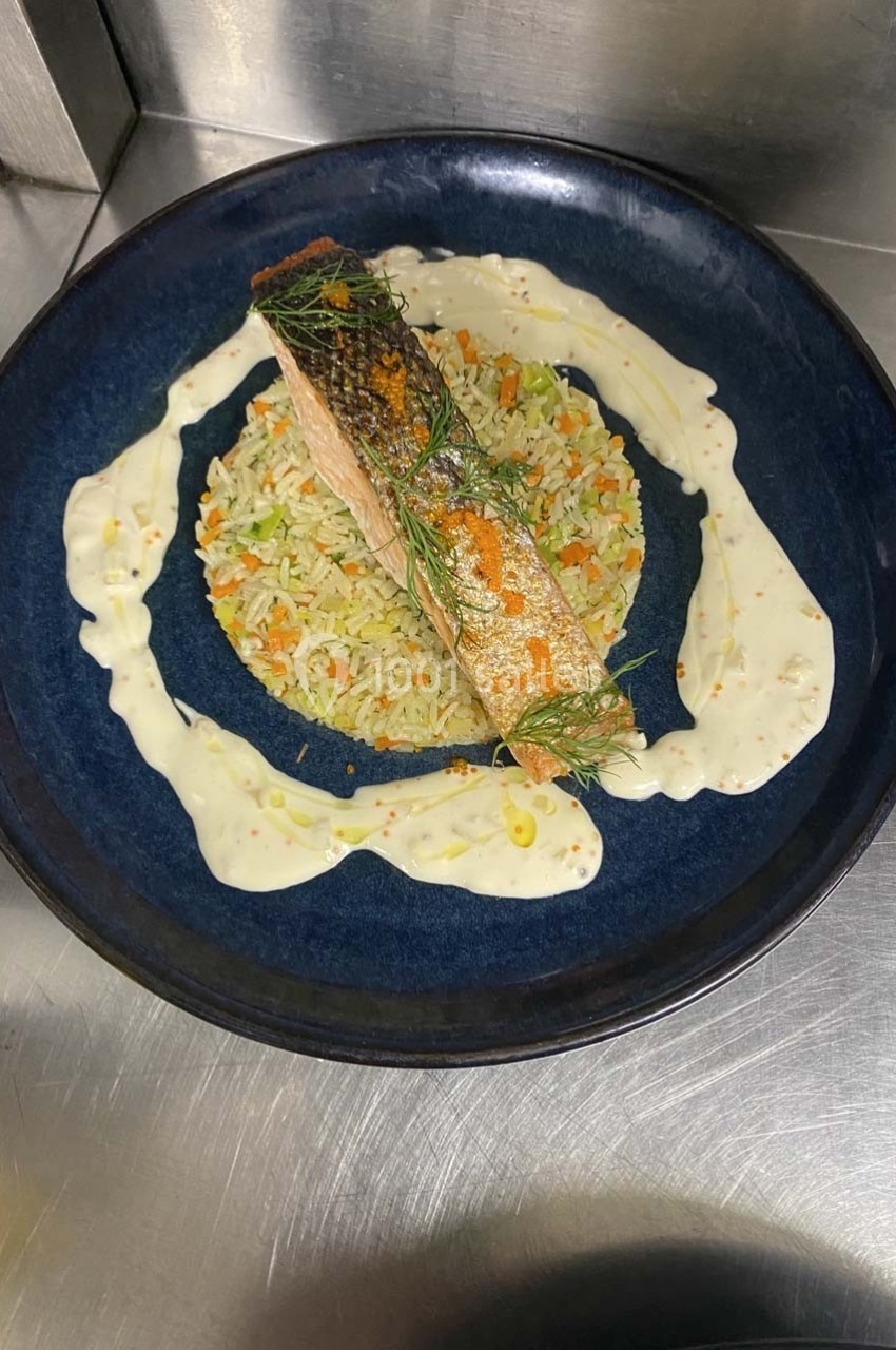 Filet de saumon grillé sur lit de riz aux légumes, entouré de sauce crémeuse et garni d'herbes fraîches.