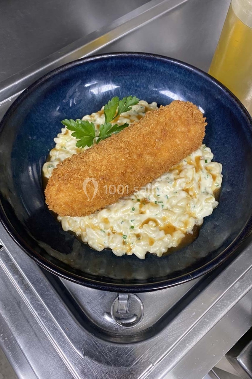 Plat composé d'une croquette dorée posée sur un risotto crémeux garni de persil, servi dans une assiette noire.