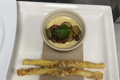 Miniature Location salle Rueil-Malmaison (Hauts-de-Seine) - Espace Laplace #28 Assiette de velouté orange garnie de croûtons dorés et de traits de crème blanche, servie sur une table en inox.