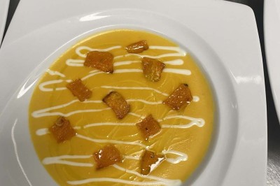 Miniature Location salle Rueil-Malmaison (Hauts-de-Seine) - Espace Laplace #31 Assiette de velouté orange garnie de croûtons dorés et de traits de crème blanche, servie sur une table en inox.