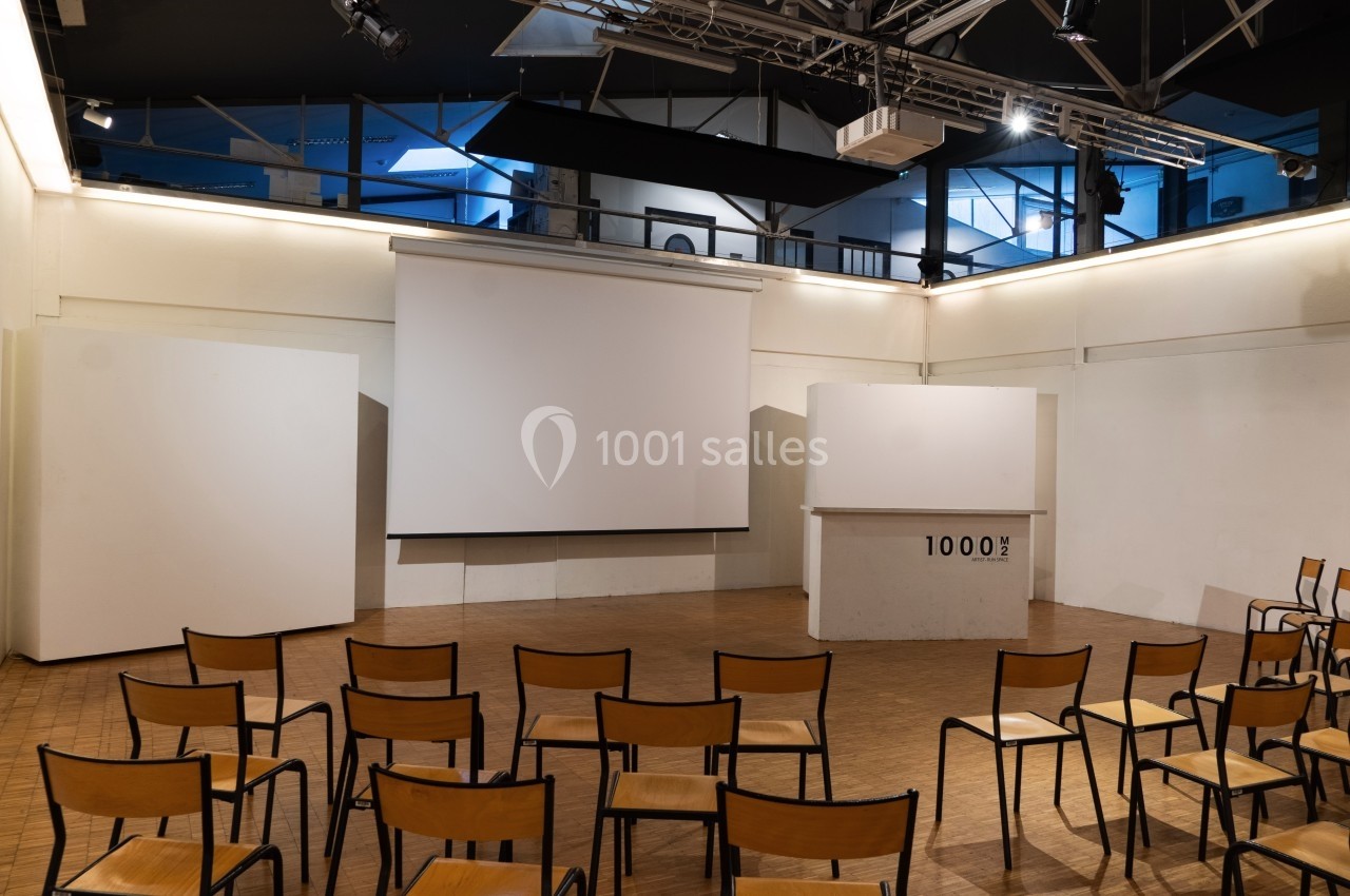 Salle avec des chaises alignées face à un écran de projection et un pupitre, éclairée par des lumières artificielles.