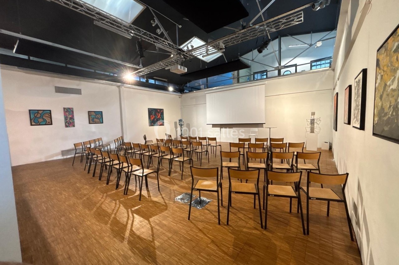 Salle lumineuse avec des chaises disposées en rangées face à un écran de projection, murs ornés de peintures.