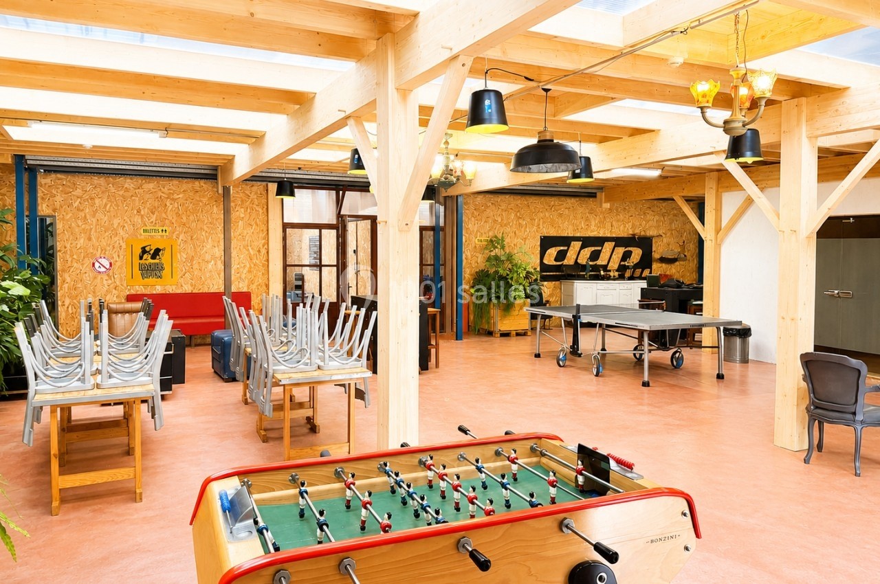 Salle lumineuse avec baby-foot, tables empilées, baby-foot et décoration en bois et métal.