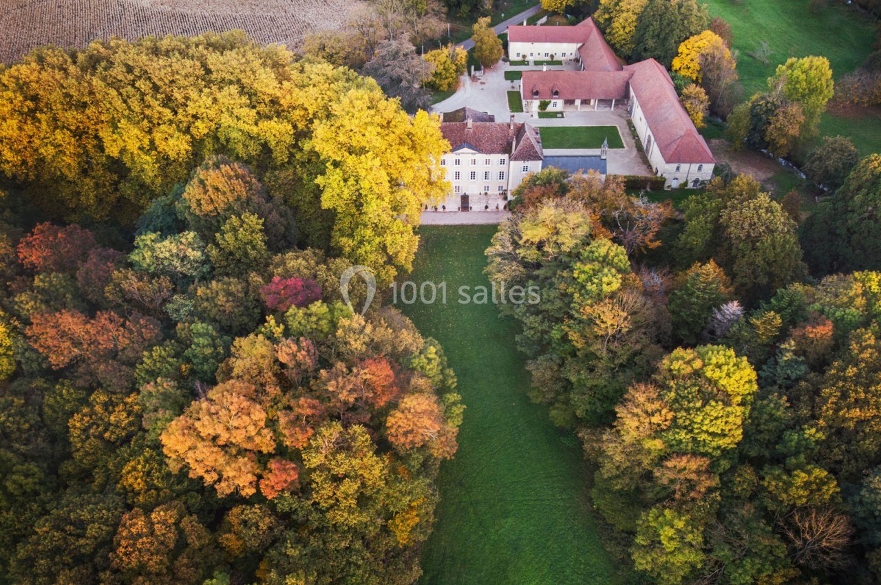 Vue aérienne d'un domaine entouré d'arbres aux couleurs automnales, avec bâtiments et pelouse centrale.