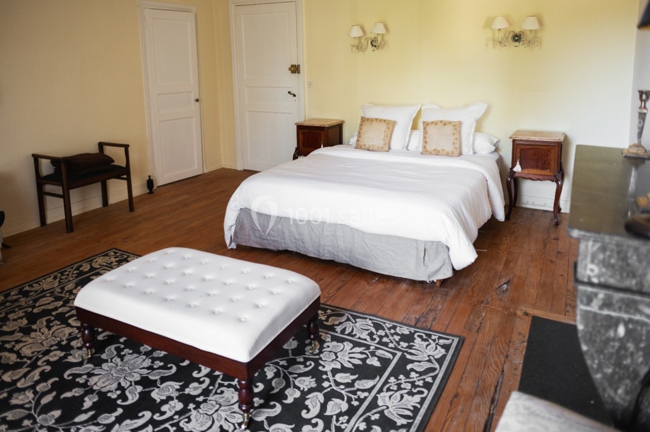 Chambre lumineuse avec lit double, banc capitonné, tapis à motifs et meubles en bois sur un parquet.