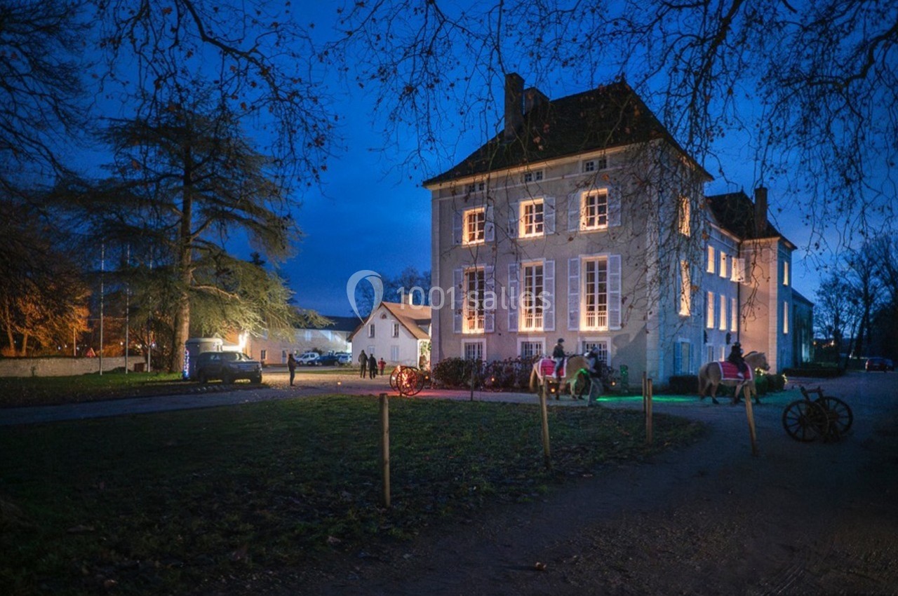 Façade éclairée d'un bâtiment ancien entouré d'arbres, avec des visiteurs et des calèches en soirée.
