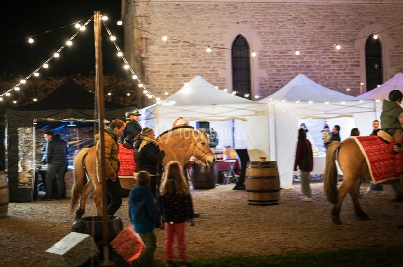 Des enfants observent des cavaliers sur des chevaux près de stands éclairés et d'une église en soirée.