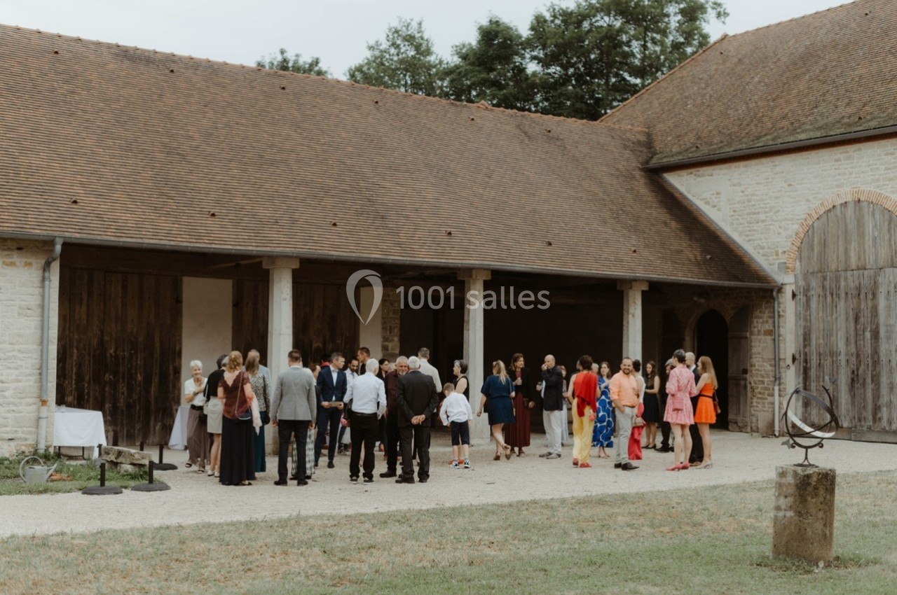 Groupe de personnes discutant dans une cour pavée devant un bâtiment en pierre avec des portes en bois.