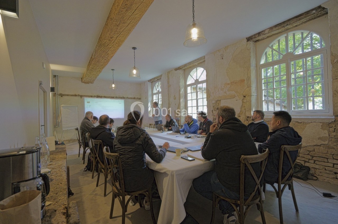 Un groupe de personnes assises autour d'une table dans une salle lumineuse, assistant à une présentation projetée au mur.