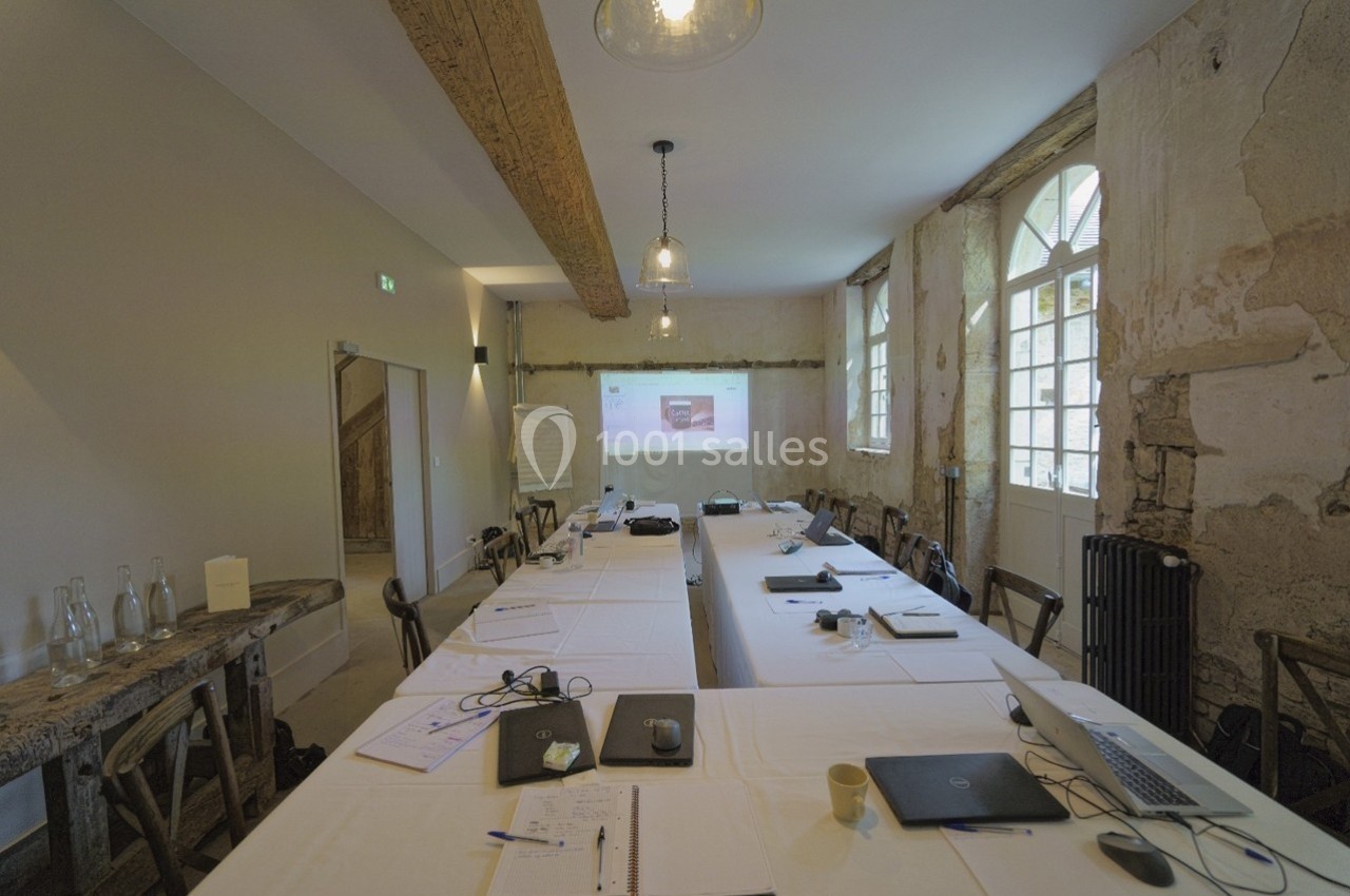 Salle de réunion rustique avec murs en pierre, grande table rectangulaire, ordinateurs portables et projecteur allumé.