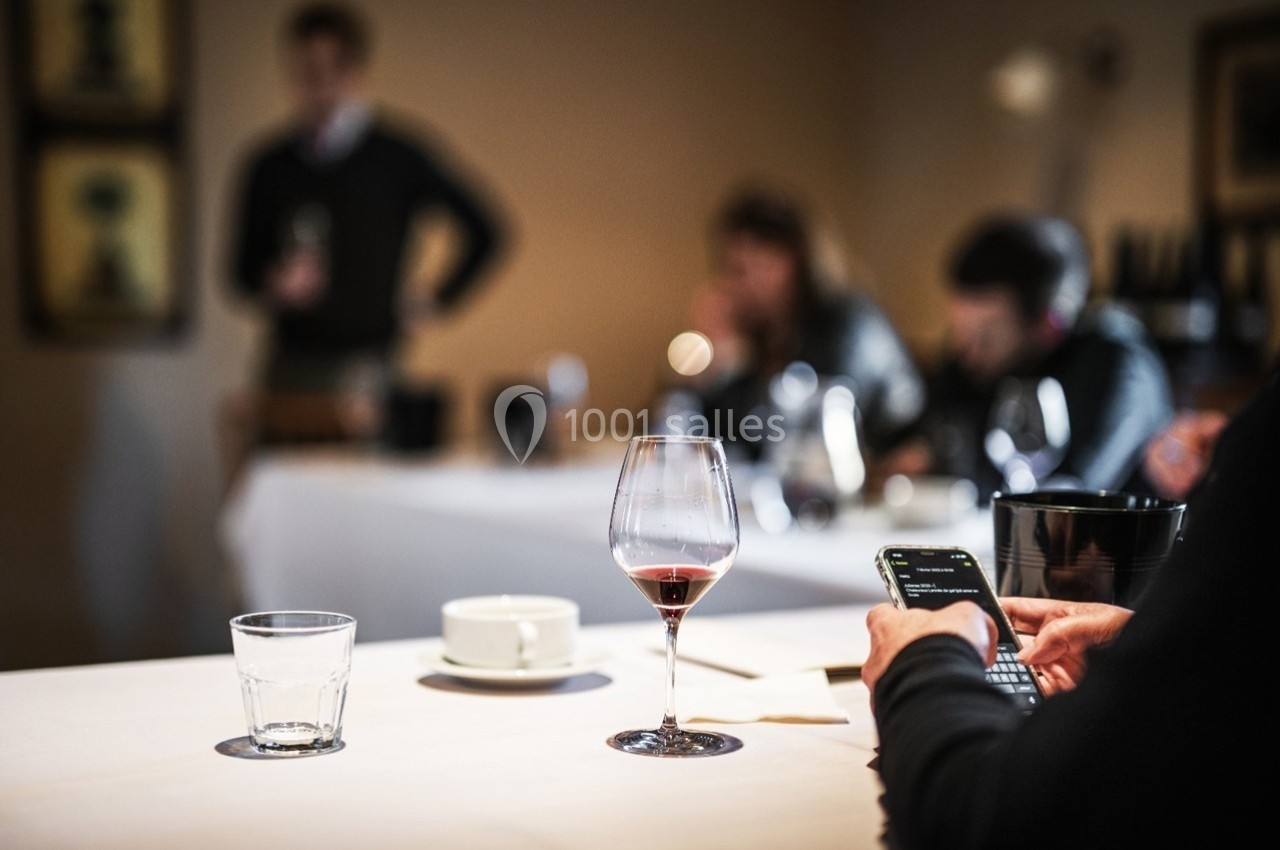 Un verre de vin rouge sur une table, avec des personnes floues en arrière-plan dans une ambiance de réunion.