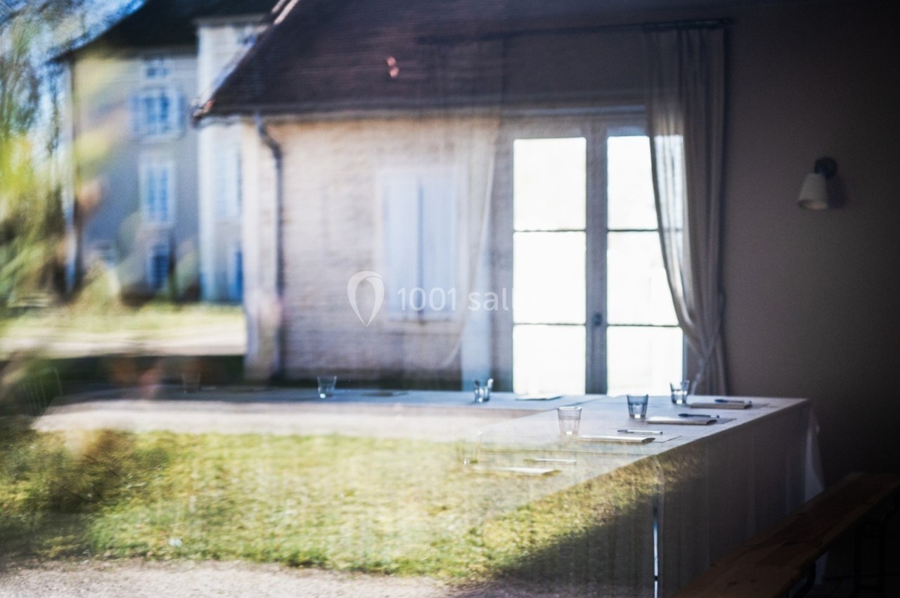 Reflet d'une table dressée avec des verres dans une salle, visible à travers une fenêtre donnant sur un jardin.