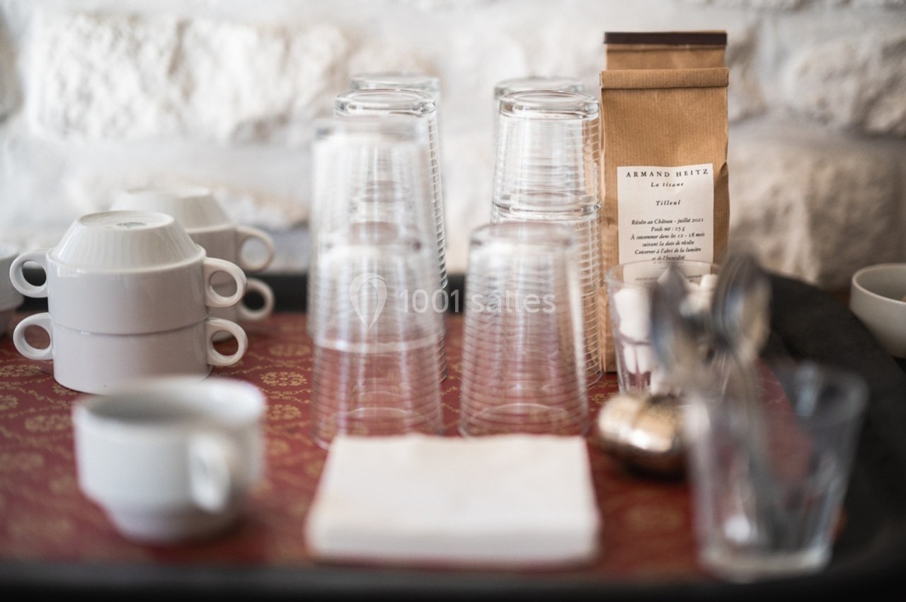 Verres empilés, tasses blanches et sachet de café disposés sur un plateau avec une nappe rouge.