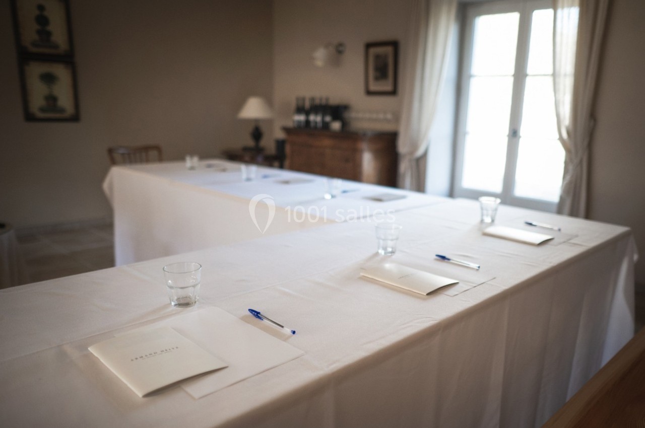 Salle de réunion lumineuse avec tables disposées en U, stylos et documents posés sur des nappes blanches.