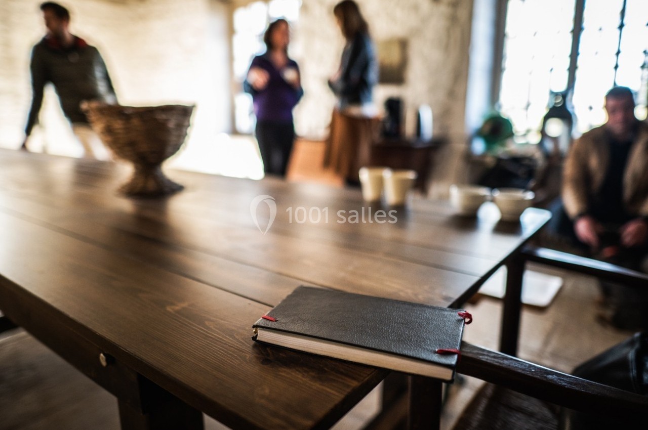 Carnet noir posé sur une table en bois, avec des personnes floues en arrière-plan dans une pièce lumineuse.