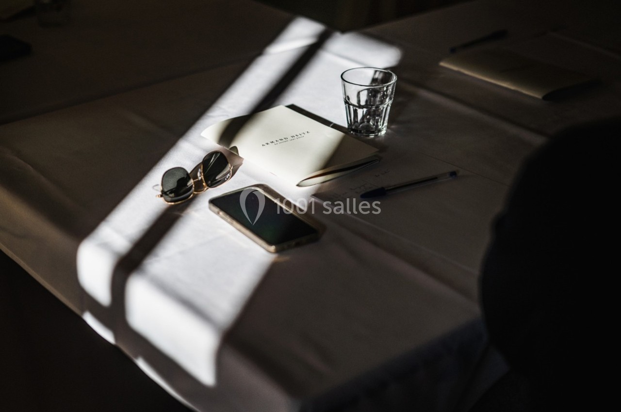 Objets sur une table éclairée par une lumière naturelle : lunettes de soleil, carnet, stylo, verre et smartphone.