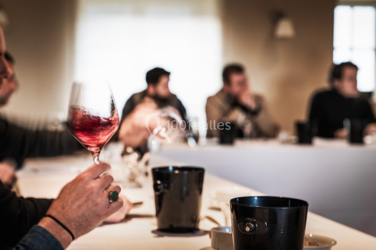 Une personne tient un verre de vin rouge lors d'une dégustation dans une salle avec plusieurs participants.
