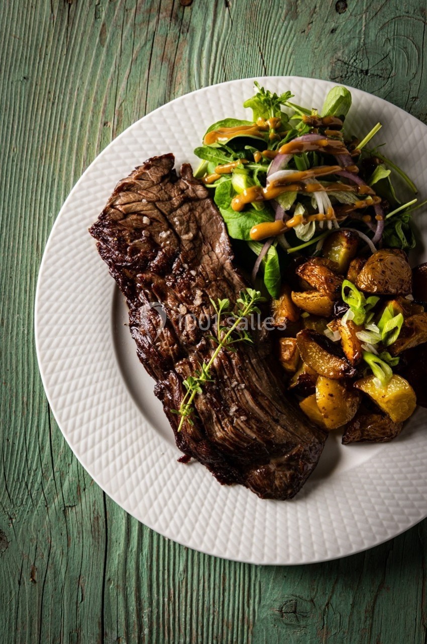 Assiette avec un steak grillé, des pommes de terre rôties et une salade verte garnie de sauce, sur une table en bois.
