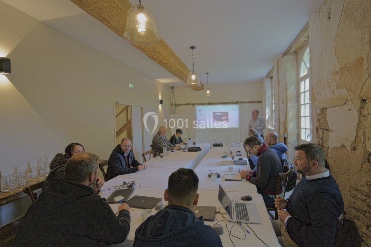 Personnes assises autour d'une table en réunion, avec un présentateur projetant des informations sur un écran.