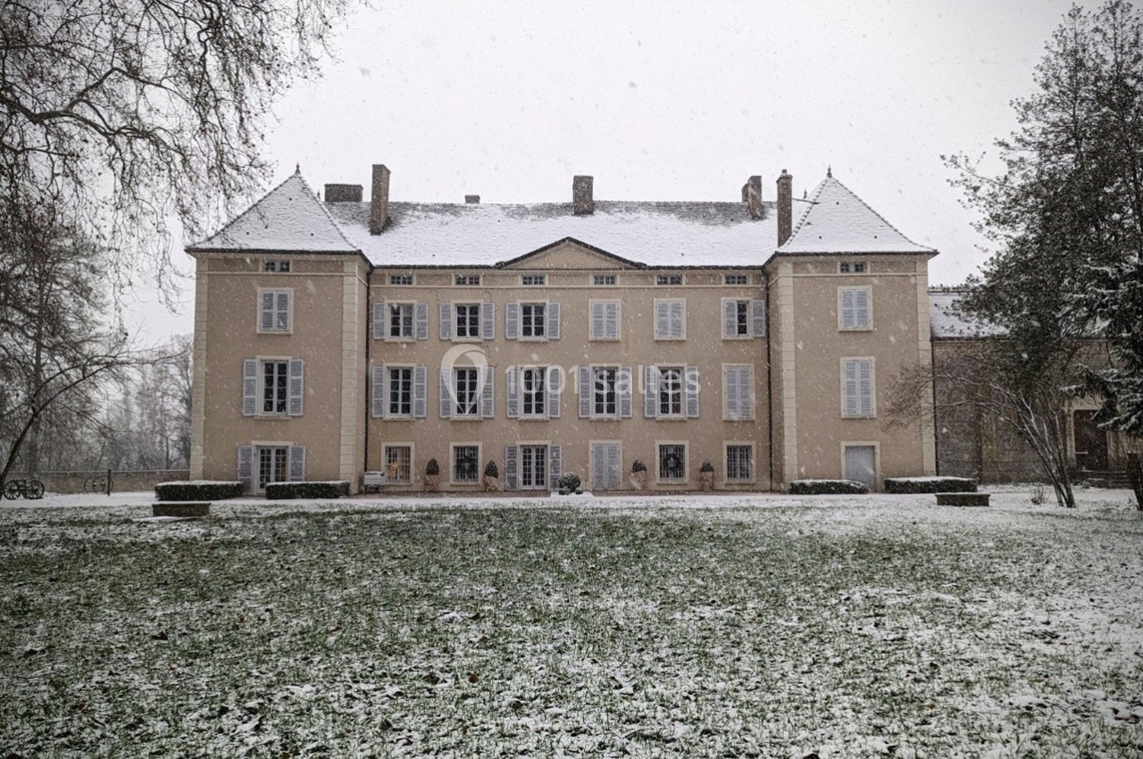 Façade d'un grand bâtiment ancien entouré d'arbres, avec un jardin enneigé au premier plan.