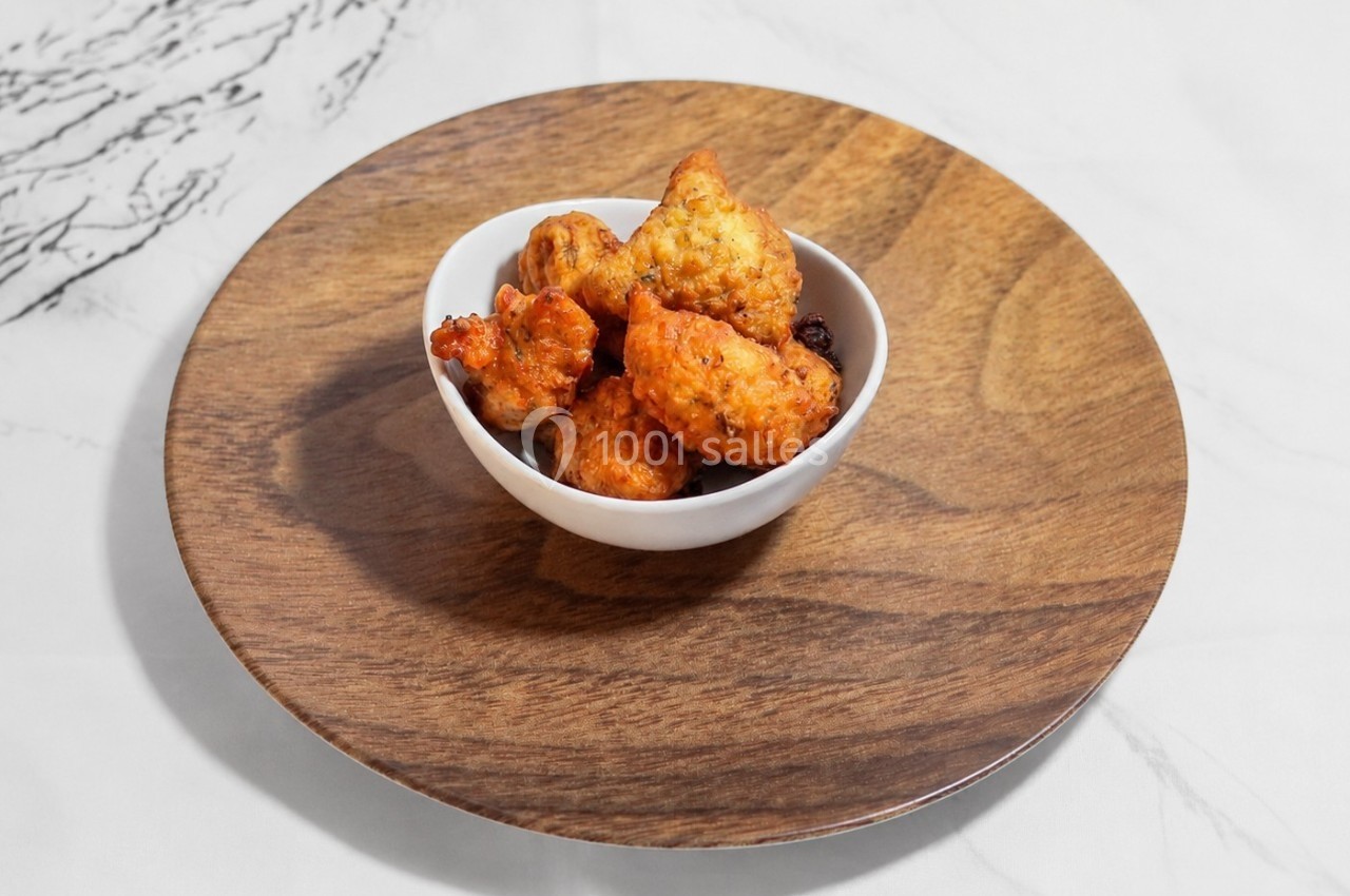 Bol de beignets dorés posés sur une assiette en bois, sur une surface en marbre blanc.