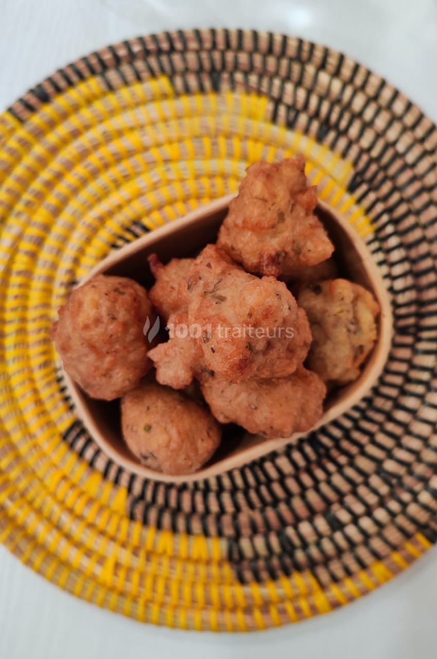 Beignets dorés servis dans un récipient en bois, posés sur un plateau tressé aux motifs jaunes et noirs.