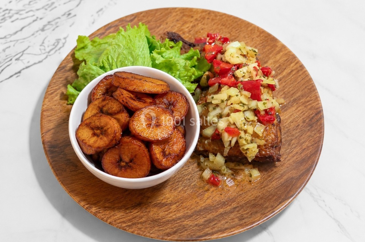 Assiette en bois contenant des bananes plantains frites, une salade verte et une viande garnie de légumes colorés.